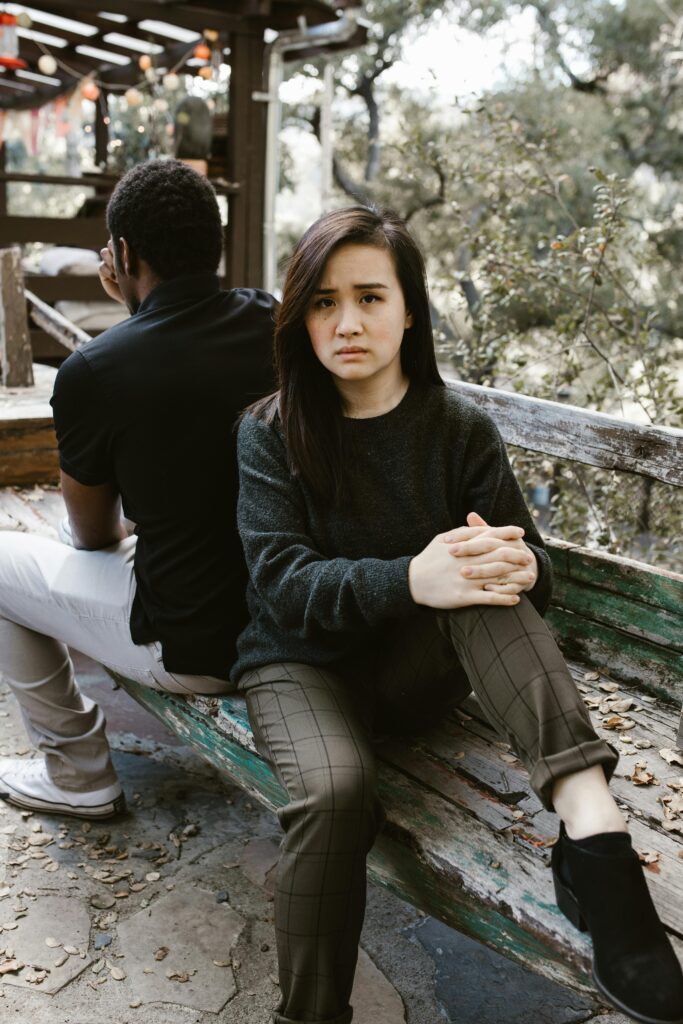 A couple sits back-to-back on a bench, expressing tension and conflict.